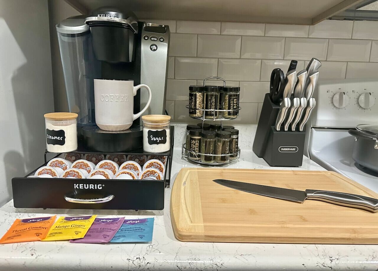 A kitchen counter with a Keurig coffee maker, a coffee mug, a cutting board, a knife, a spice rack, and a knife block.