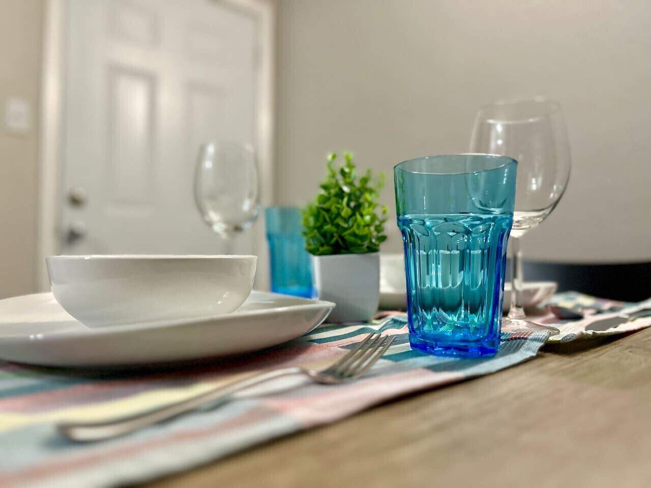 A dining table with a white plate, a blue glass, and a fork.