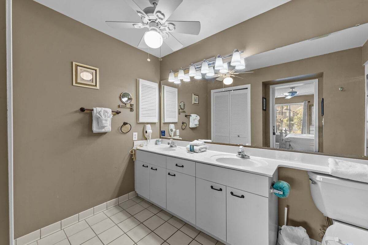 Un bagno con ventilatore a soffitto, due lavabi, uno specchio grande e mobiletti bianchi.