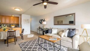 A modern living room with a sofa, coffee table, and dining area. - Luxury Maui Condo Ocean Views Resort Perks (Kihei)