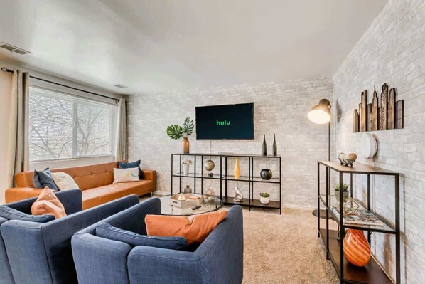 A modern living room with a sofa, armchairs, a coffee table, a TV, and decorative items on shelves. - Convenient 2BR Apt w/ Parking, Near Downtown SLC (Salt Lake City)