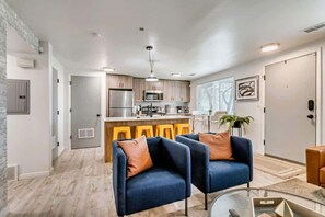 A modern kitchen with a central island, bar stools, and a dining area with a blue sofa and a glass coffee table. - Convenient 2BR Apt w/ Parking, Near Downtown SLC (Salt Lake City)