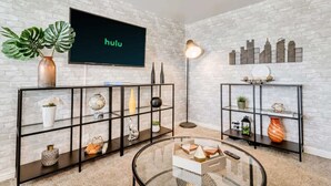 A modern living room with a flat-screen TV, two black shelving units, a glass coffee table, and a floor lamp. - Convenient 2BR Apt w/ Parking, Near Downtown SLC (Salt Lake City)