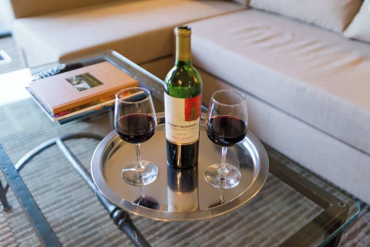 A bottle of wine on a tray with two glasses of red wine, a book, and a sofa in the background.