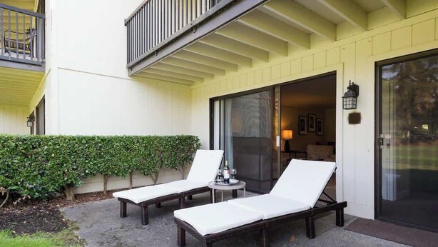 Een balkon met twee witte lounge fauteuils en een tafeltje met een fles en glazen.