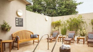 Een terras buiten met een zwembad, houten meubels en potplanten.