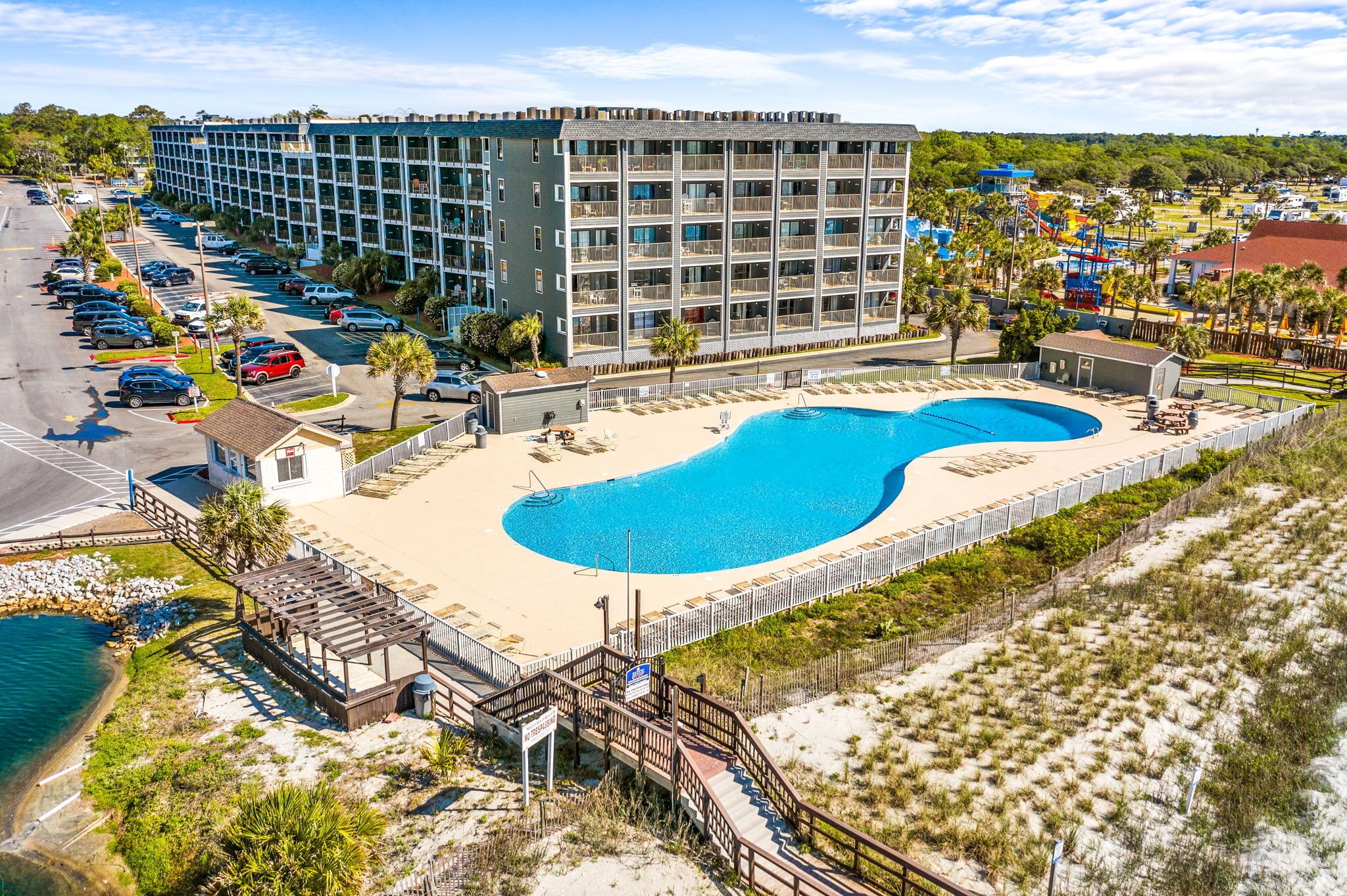 A hotel with a large pool, a parking lot, and a beach area.