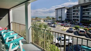 A balcony with chairs, a view of a parking lot, and a building with multiple floors. - Myrtle Beach Resort A 210 (Myrtle Beach)