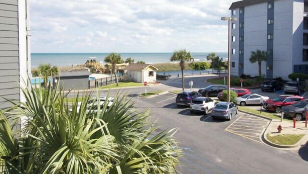 A parking lot with cars, a building, and a beach in the background. - Myrtle Beach Resort A 210 (Myrtle Beach)