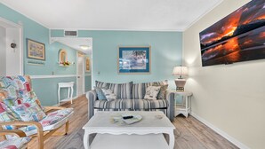 A living room with a striped sofa, a patterned armchair, a white coffee table, and a wall-mounted TV. - Myrtle Beach Resort A 210 (Myrtle Beach)