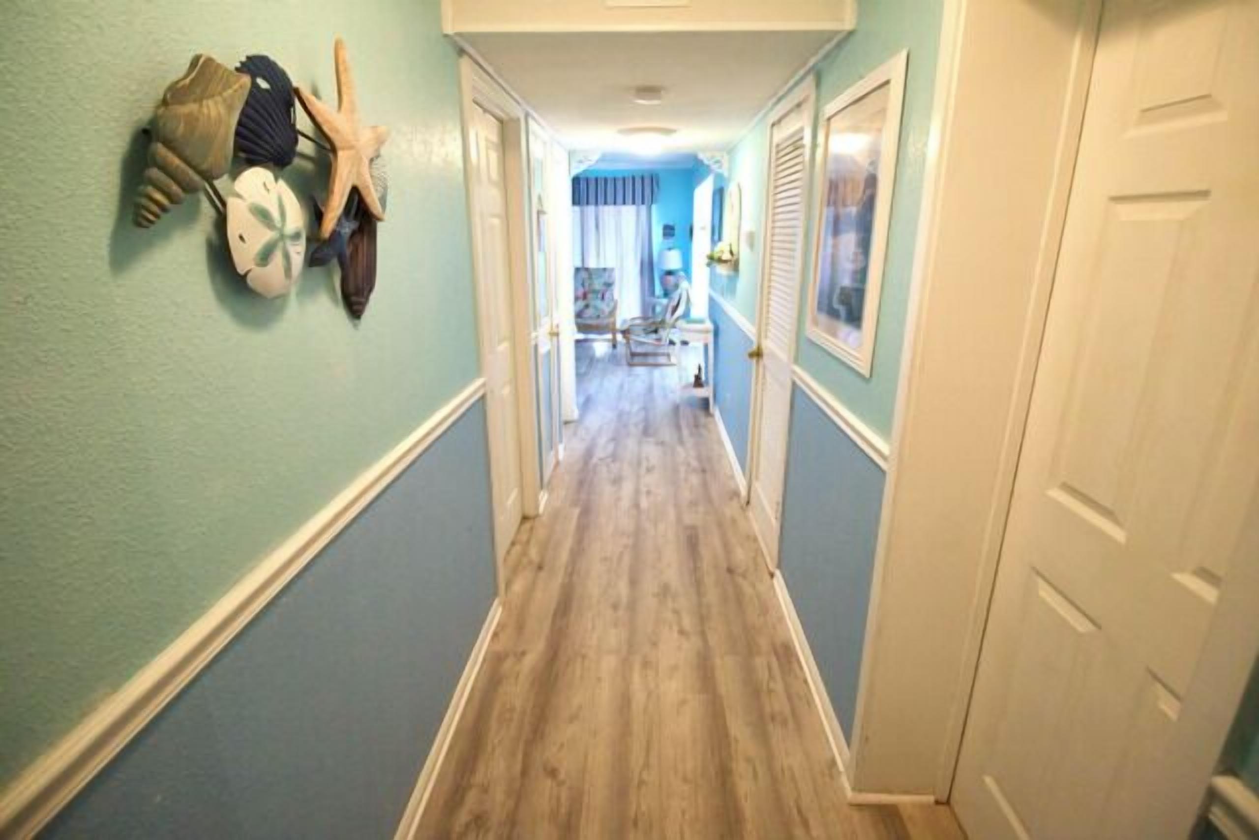 A hallway with a wooden floor, light blue walls, and a door on the right.