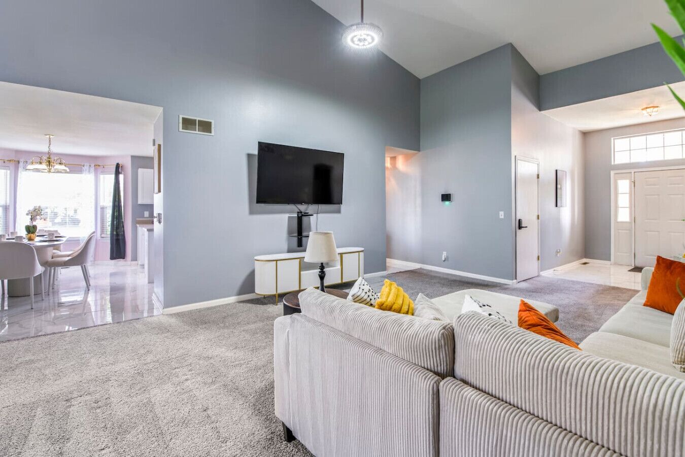 Un salon moderne avec un mur gris, un téléviseur à écran plat, un canapé blanc et un coin repas comprenant une table et des chaises.