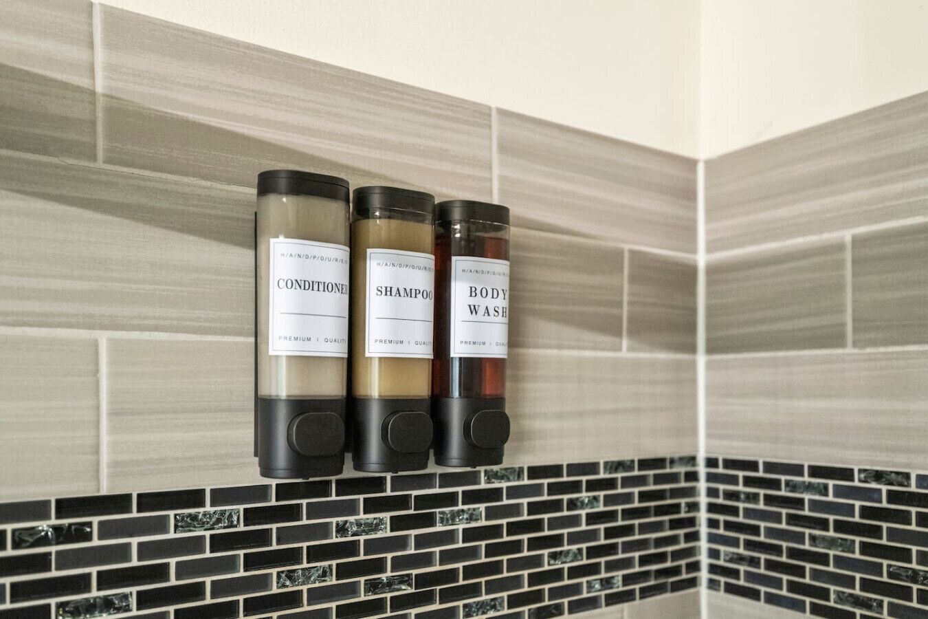 Ein Badezimmer mit drei Spendern, auf denen 'CONDITIONER', 'SHAMPOO' und 'BODY WASH' stehen.