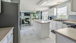 A modern kitchen with white cabinets, a central island, and a dining area with a green sofa and white chairs. - Modern Comfort Loves Park Stylish 3BR Getaway (Loves Park)