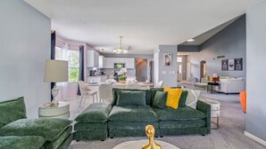 A modern living room with a green sectional sofa, a round coffee table, and a dining area in the background. - Modern Comfort Loves Park Stylish 3BR Getaway (Loves Park)