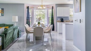 A modern dining area with a marble floor, a round table with chairs, a chandelier, and a view of the outdoors through large windows. - Modern Comfort Loves Park Stylish 3BR Getaway (Loves Park)