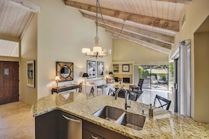 A kitchen with granite countertops, stainless steel sinks, and a hanging light fixture.