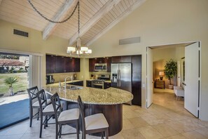 A modern kitchen with granite countertops, dark wood cabinets, stainless steel appliances, and a large island with bar stools.