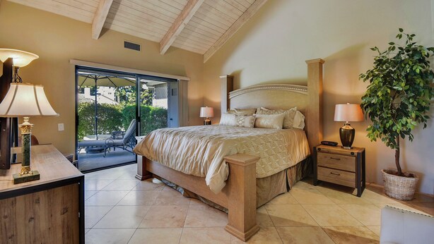 A bedroom with a bed, bedside tables, a lamp, a potted plant, and a view of the outdoors. - Elegant Lakeside Villa (Rancho Mirage)