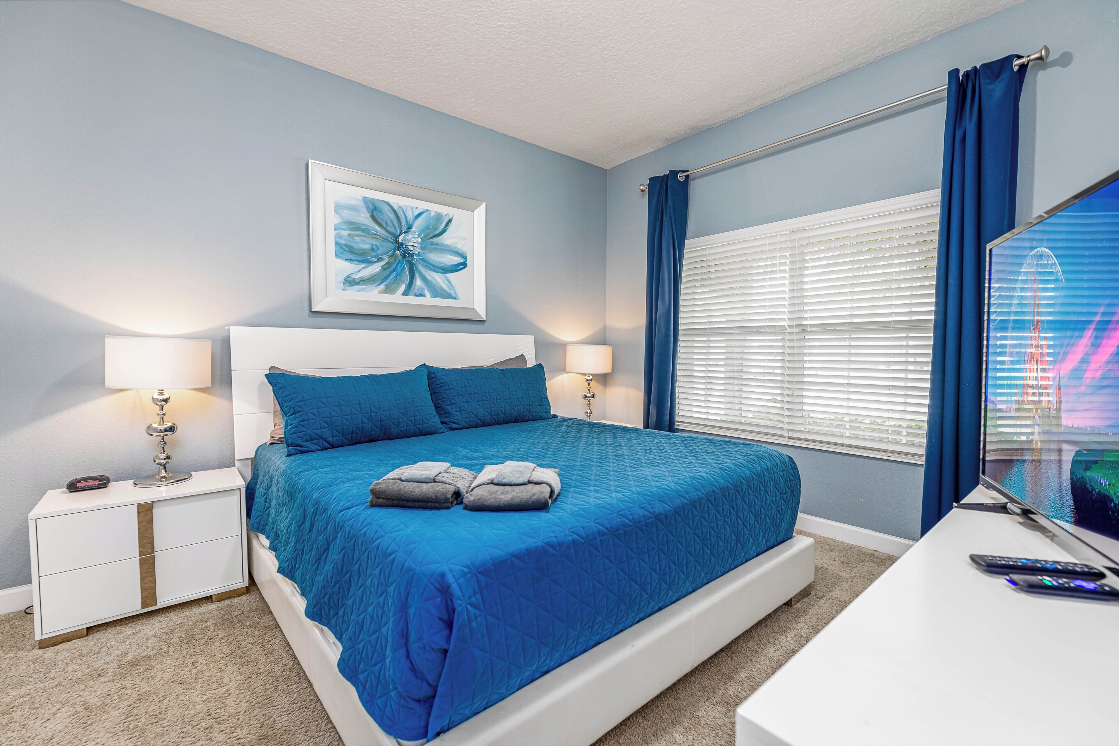 A bedroom with a large bed, two bedside tables, a TV, and a window with curtains.