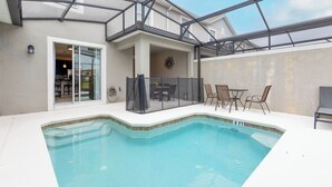 A swimming pool with a glass enclosure, a patio area with chairs, and a view of the interior of the building. - Tvpm-4885rc/sl (Kissimmee)
