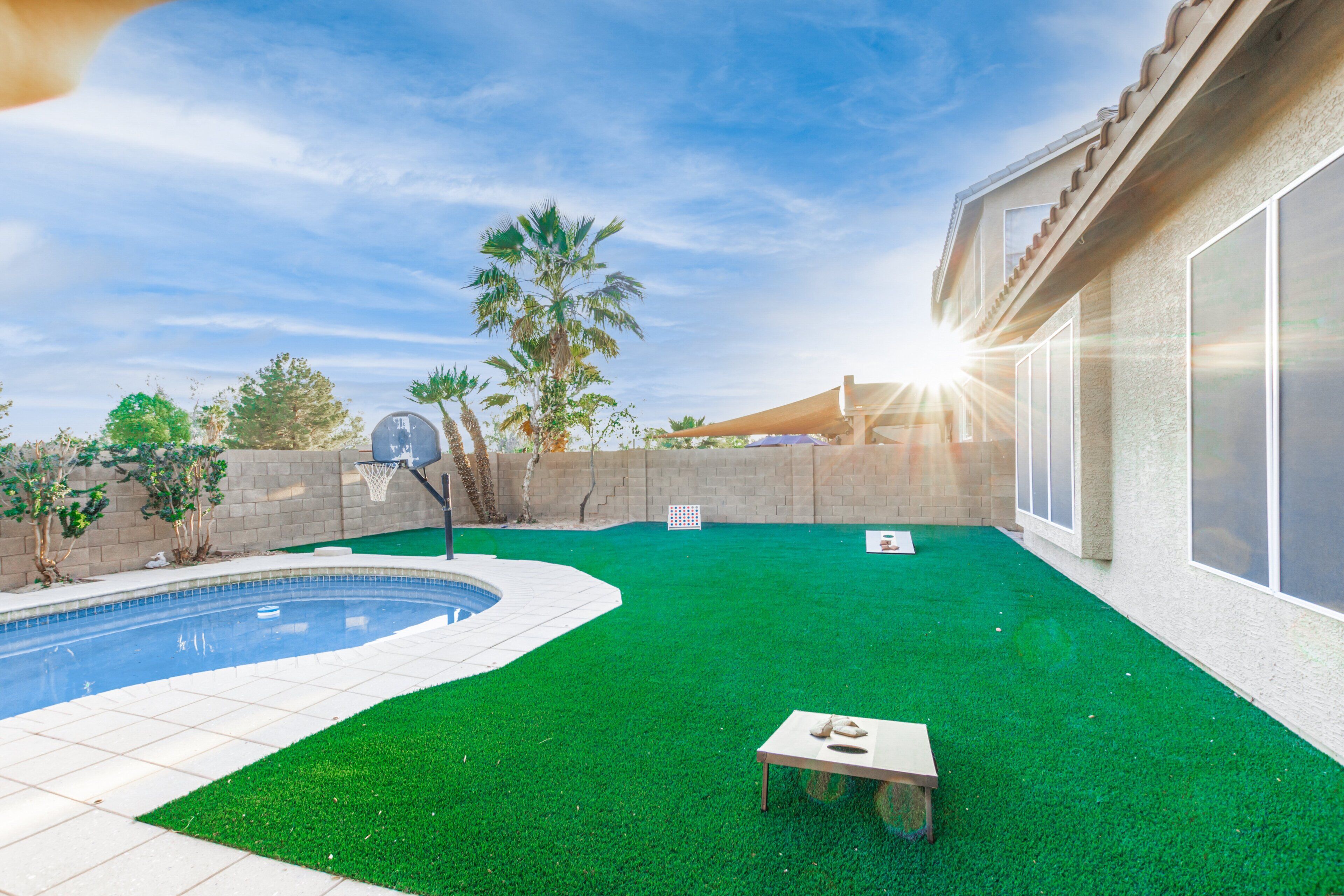 A backyard with a swimming pool, artificial grass, a basketball hoop, and a table.