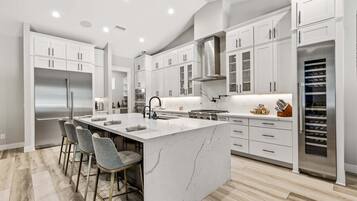 A modern kitchen with white cabinets, a stainless steel refrigerator, a marble island, and bar stools.