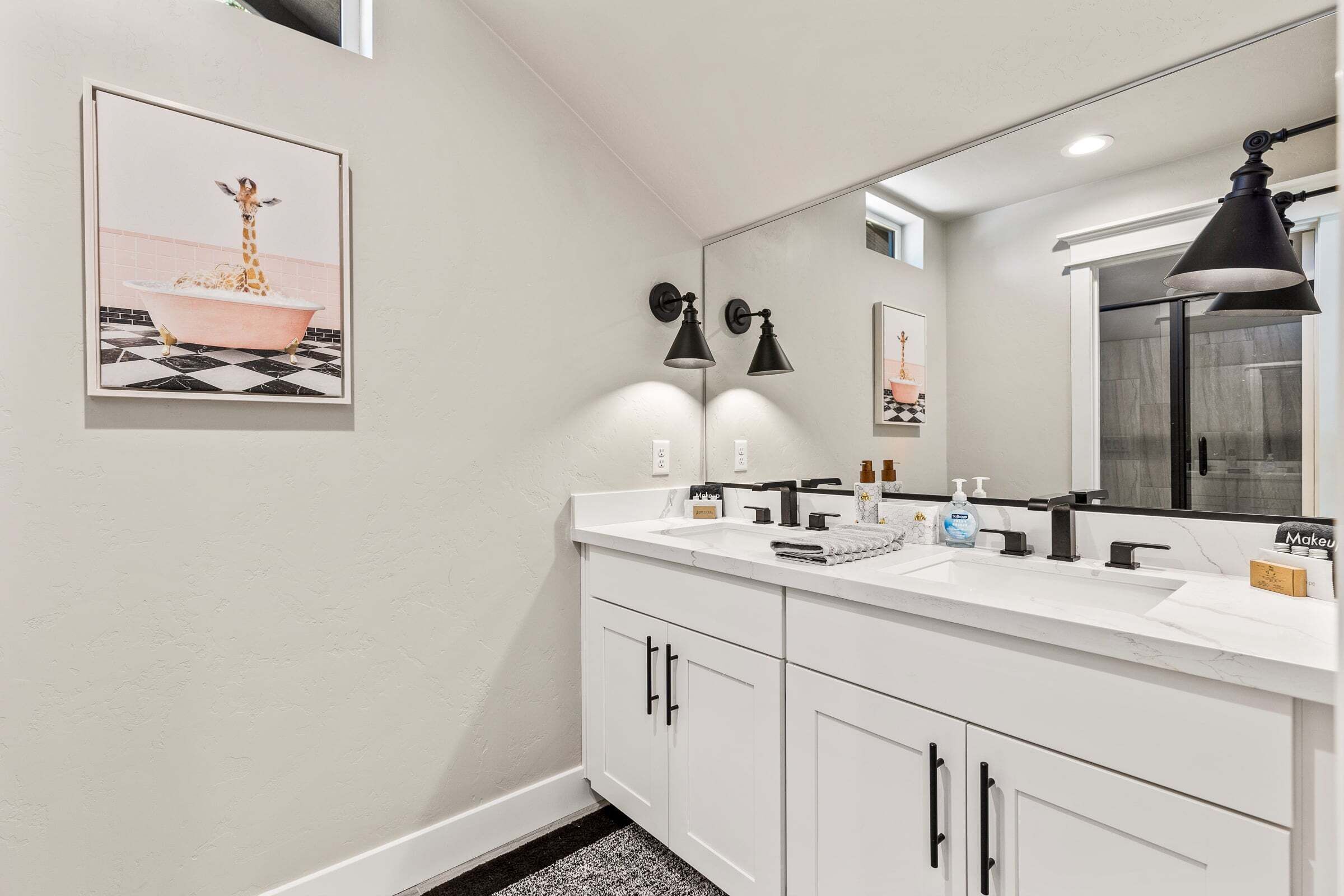 A bathroom with a white vanity, black fixtures, a large mirror, and a giraffe-themed artwork on the wall.