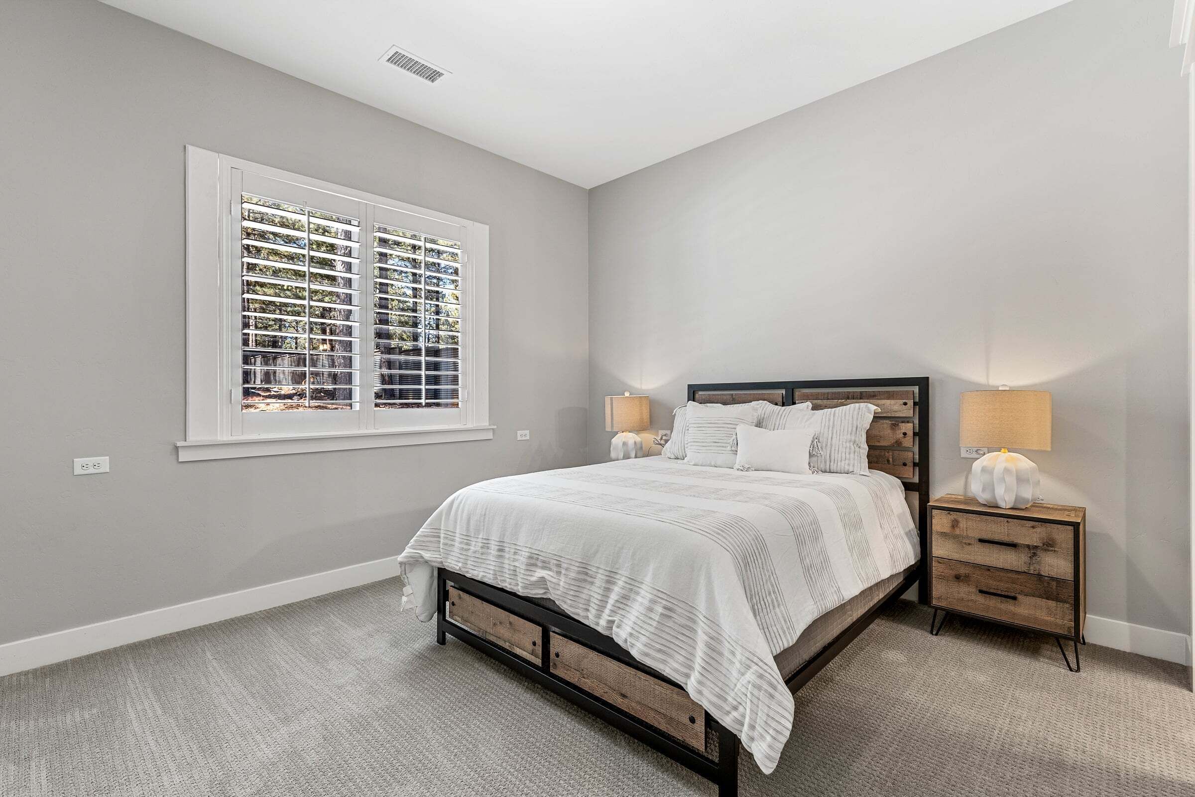 A bedroom with a bed, a nightstand, a lamp, and a window with blinds.