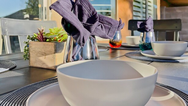 A dining table with a bowl and plates, a potted plant, and a window with shutters. - Kimberly Surprise (Surprise)