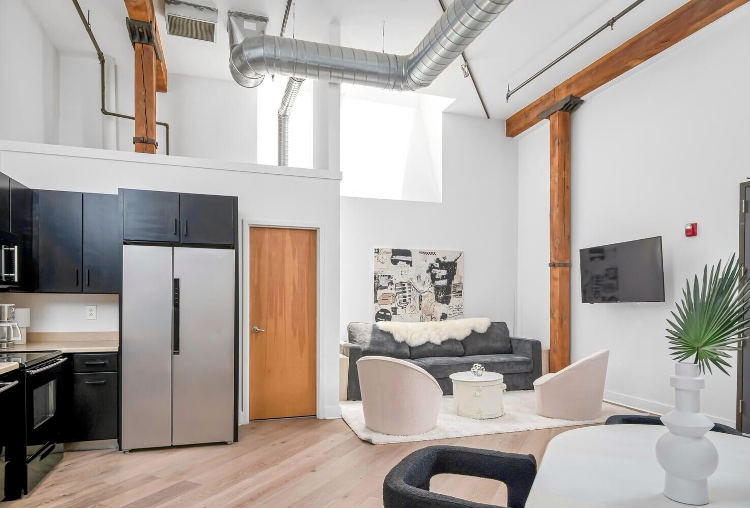 A modern kitchen with stainless steel appliances, a wooden door, and a dining area with a grey sofa and a white table.