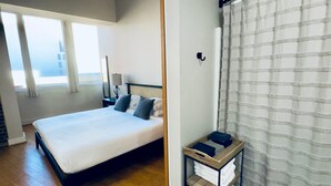 Une chambre d’hôtel avec un lit, une table de chevet, une lampe, une fenêtre avec des rideaux et un rideau de douche.