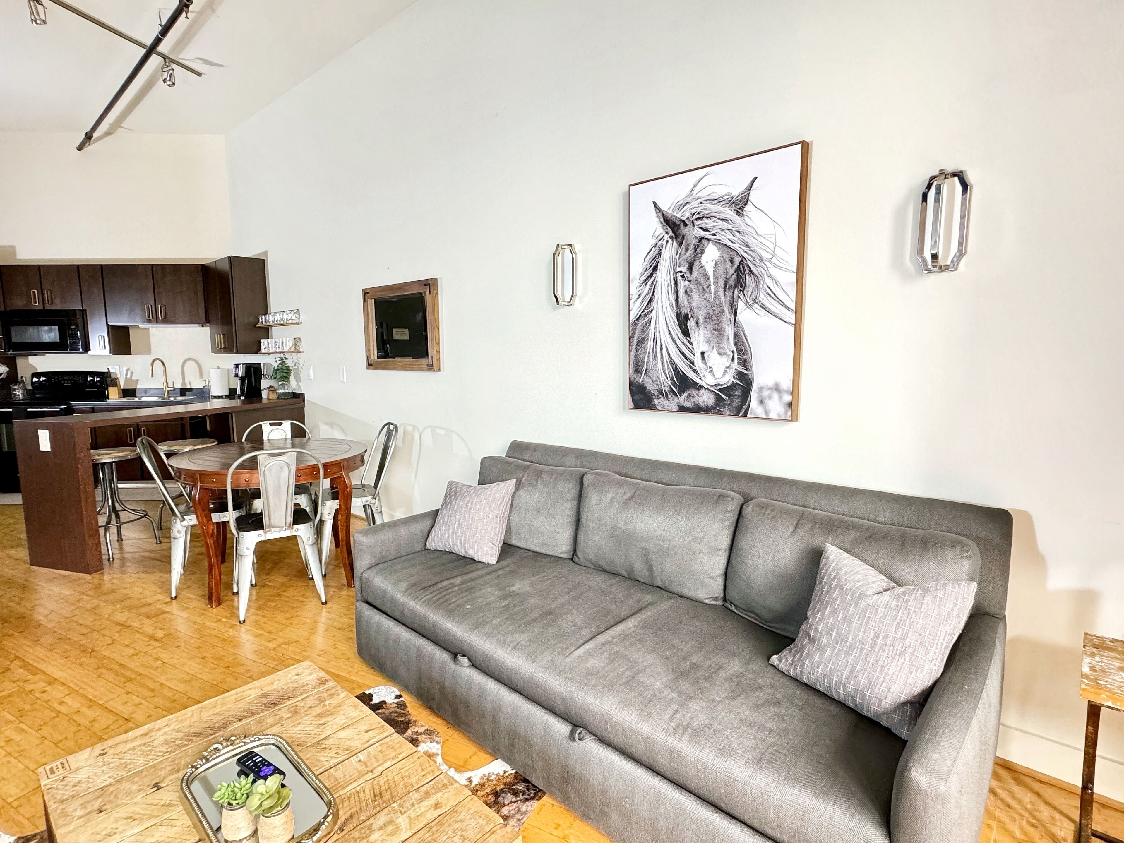 Een woonkamer met een grijze bank, een salontafel en een eethoek met een houten tafel en stoelen.