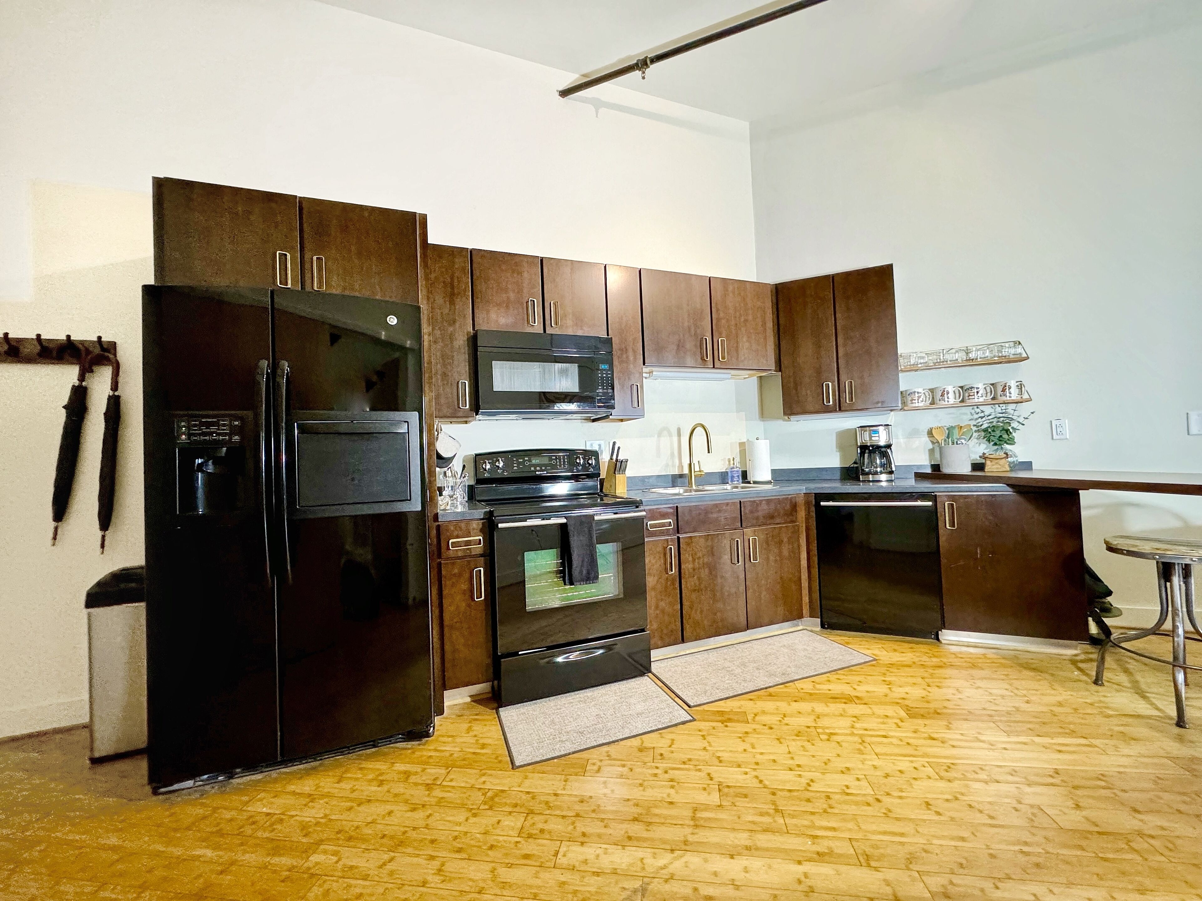 A modern kitchen with dark wooden cabinets, a black refrigerator, a microwave, an oven, and a coffee maker.