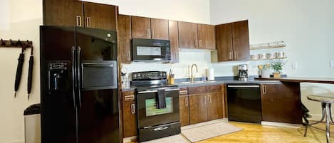 A modern kitchen with dark wooden cabinets, a black refrigerator, a microwave, an oven, and a coffee maker.