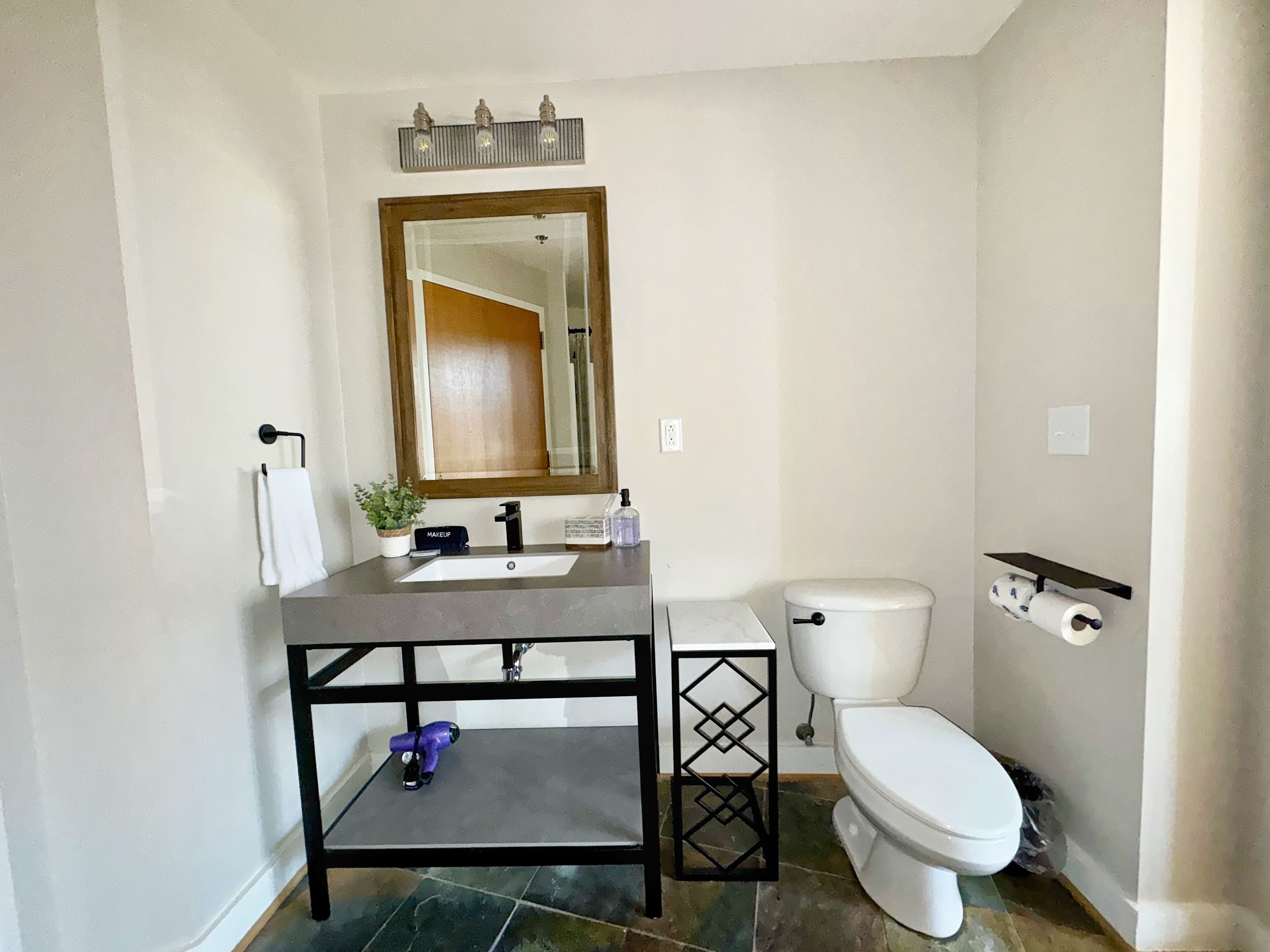 A bathroom with a sink, mirror, toilet, and a shelf with toiletries.