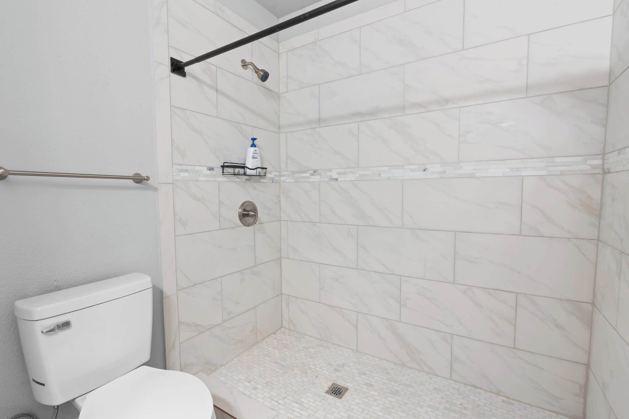 Ein Badezimmer mit Toilette, einer Dusche mit Glastür und einem Ablagefach für Pflegeprodukte.