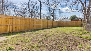 A fenced backyard with a grassy area and a house in the background. - Stylish 1-bedroom Retreat in Fort Worth (Fort Worth)