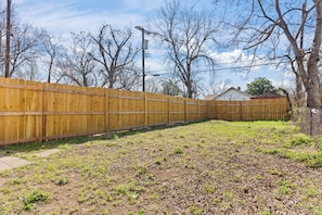 A fenced backyard with a grassy area, trees, and a house in the background. - Stylish 1-bedroom Retreat in Fort Worth (Fort Worth)
