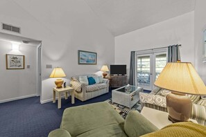 Ein Wohnzimmer mit einer Couch, zwei Lampen, einem Fernseher und einem Couchtisch.