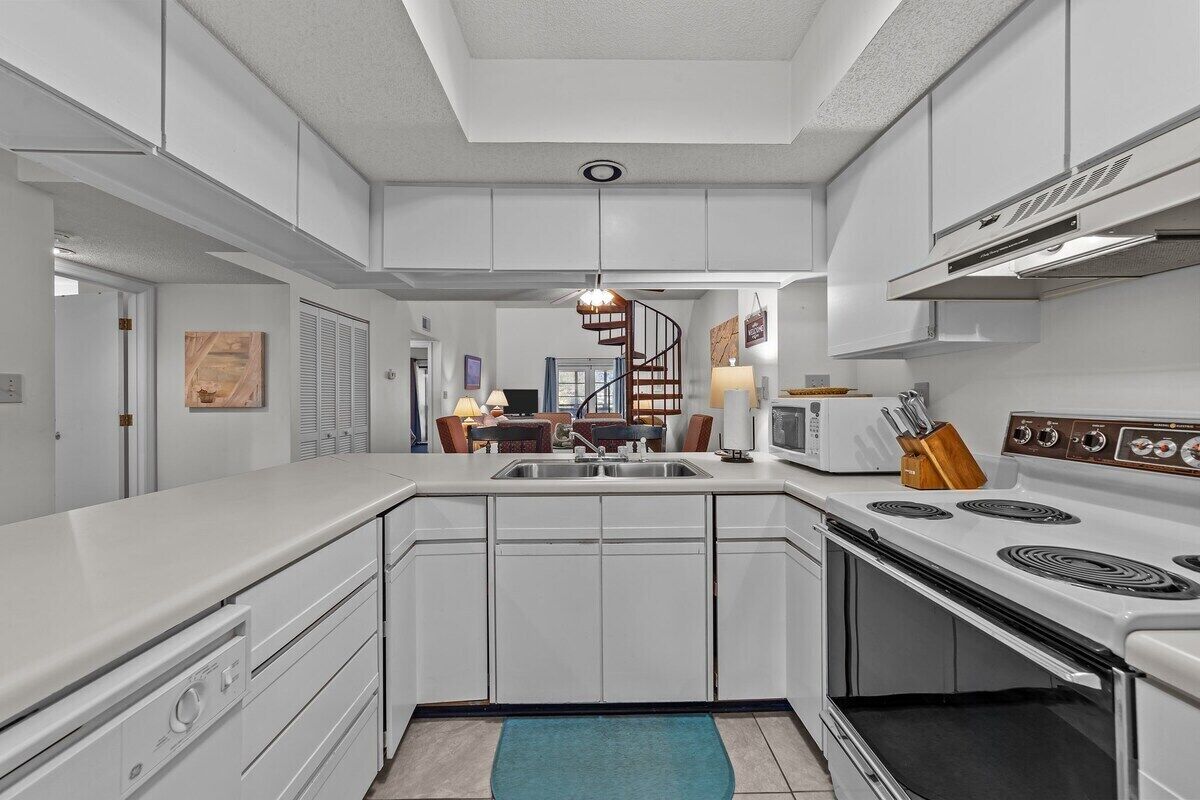 A modern kitchen with white cabinetry, a central island, a built-in stove, and a spiral staircase in the background.