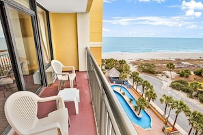 Ein Balkon mit weißen Plastikstühlen und Blick auf Strand und Pool.
