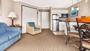 A compact living space with a sofa, a chair, a dining table with chairs, a kitchen area, and a door leading to another room. - Caravelle 706 (Myrtle Beach)