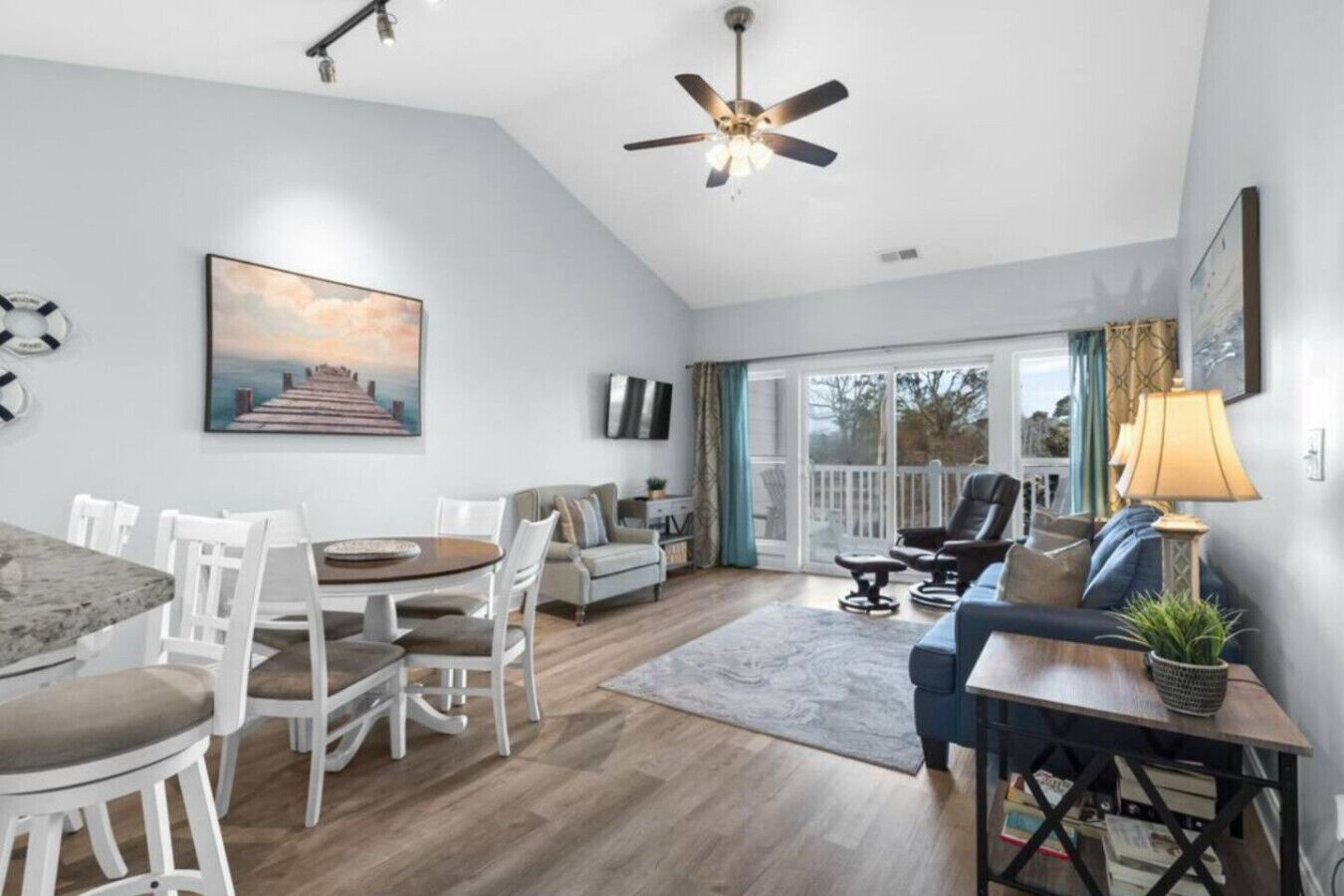 A spacious living area with a dining table, chairs, a sofa, a TV, and a ceiling fan.