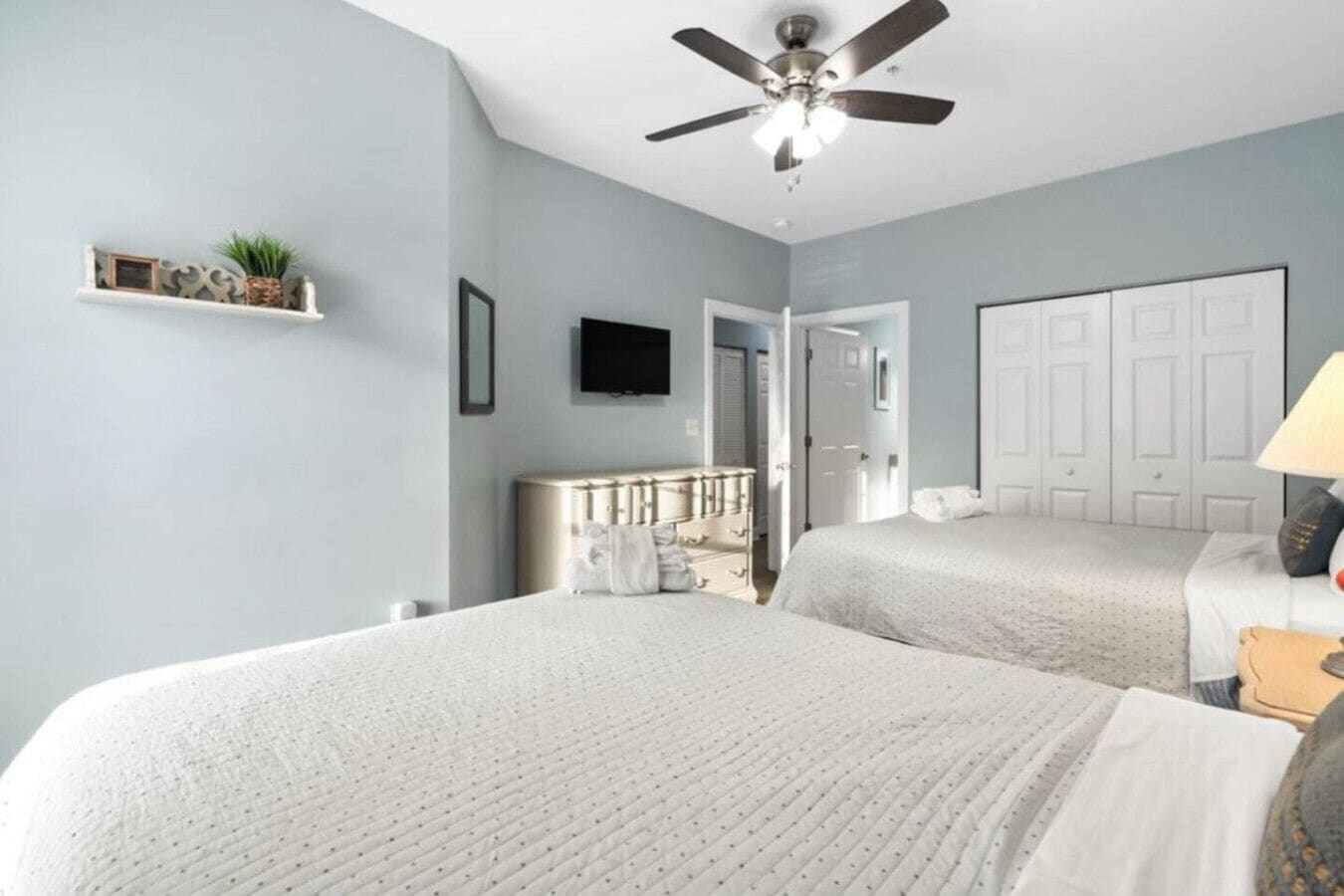 A bedroom with two beds, a ceiling fan, a TV, and a door leading to another room.