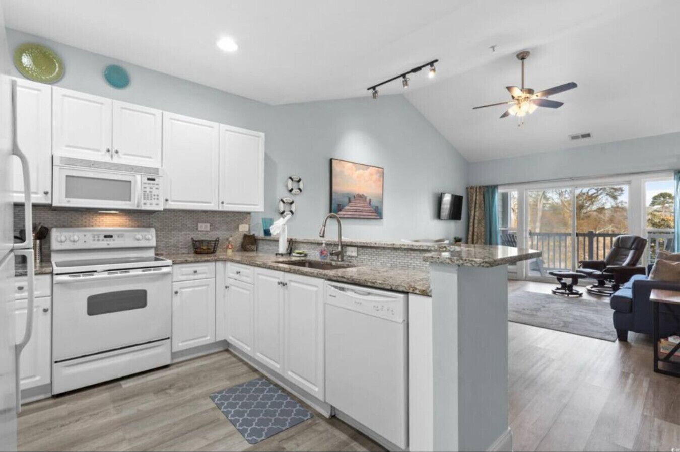 A modern kitchen with white cabinets, a built-in oven, and a microwave. There is a large island with a sink and a ceiling fan above.