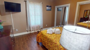 A hotel room with a bed, a TV, a window with curtains, a mirror, and a lamp. - Magnolia Pointe Luster Leaf 4837-102 (Myrtle Beach)