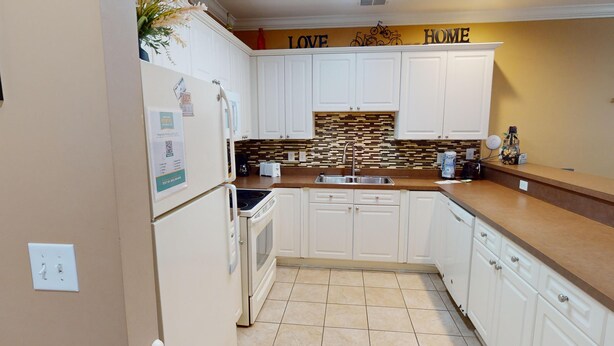 A kitchen with white cabinets, a tiled backsplash, and a countertop. There is a refrigerator, a sink, and a toaster on the counter. - Magnolia Pointe Luster Leaf 4837-102 (Myrtle Beach)