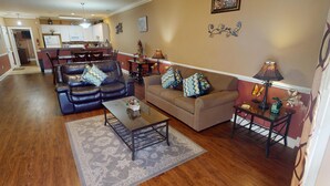 A living room with a brown sofa, a black leather couch, and a coffee table. There is a kitchen in the background with white cabinets and a microwave. - Magnolia Pointe Luster Leaf 4837-102 (Myrtle Beach)
