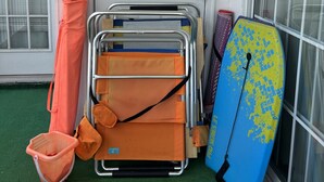 A door with a paper on it, a metal cart with orange bags, a blue surfboard, and a small orange basket. - Captains Quarters Bright 2BR Pet-friendly Beach Condo w/ Coastal Decor & Relaxed Vibes (Myrtle Beach)